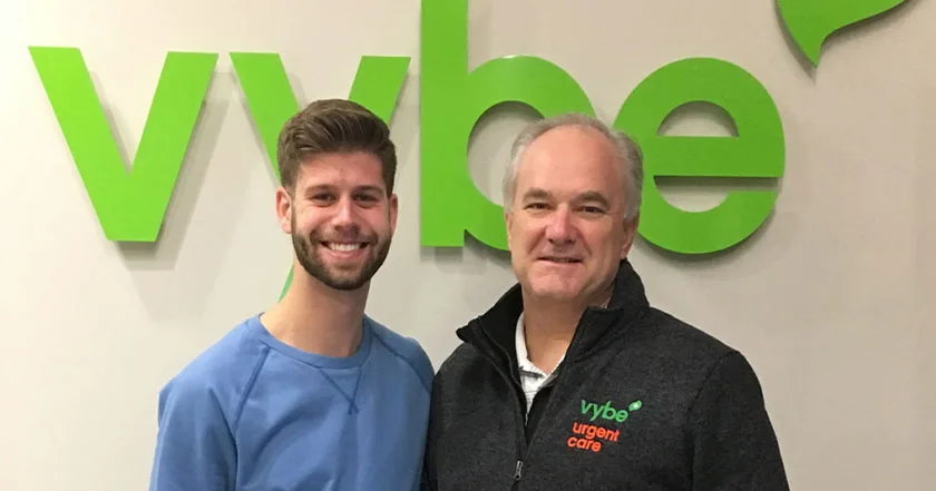 An image of a vybe urgent care doctor smiling with a patient in the patient waiting room.