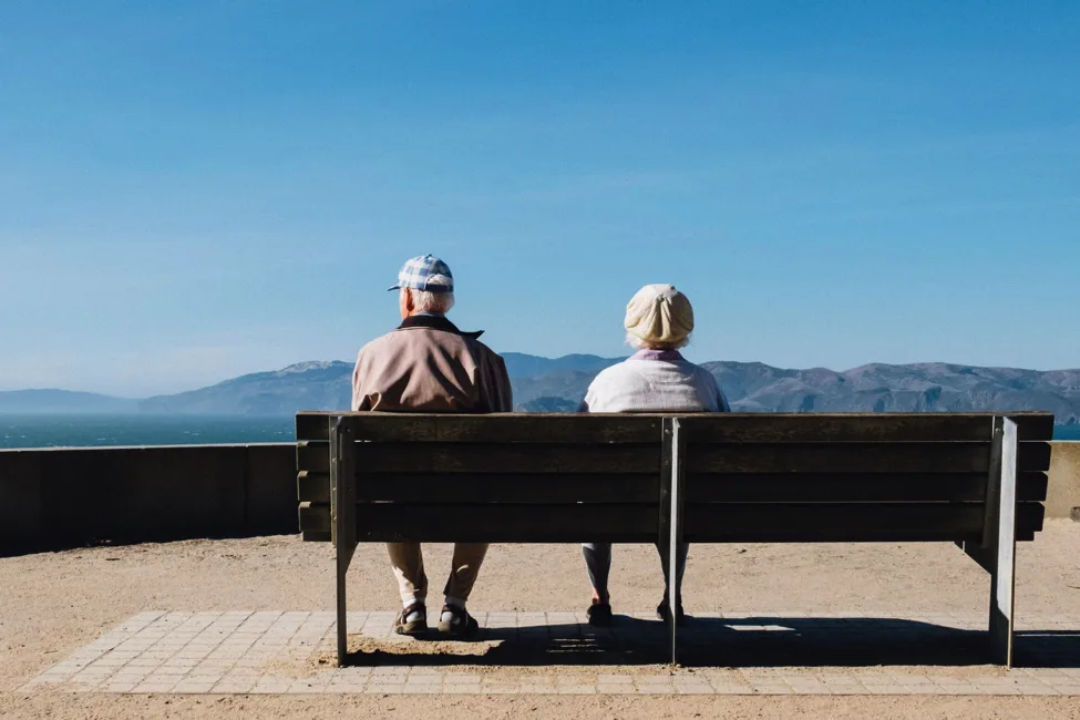 An older couple sitting on a bench outdoors.