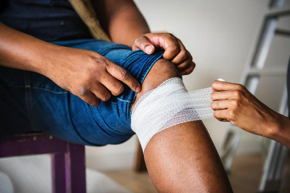 An image of a vybe urgent care patient having first aid gauze applied around his knee due to having an injury.