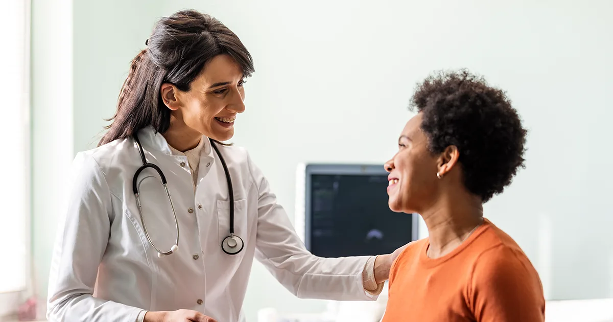 A vybe urgent care doctor comforting a female patient with a smile.
