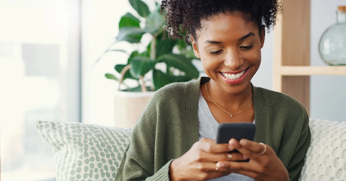 An enlarged image of a woman smiling at the news she's found on her phone that vybe urgent care accepts the UnitedHealthcare Community Plan.