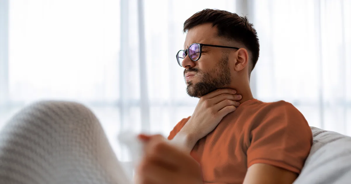 An image of a future vybe urgent care male holding his neck in pain due to having a sore throat.