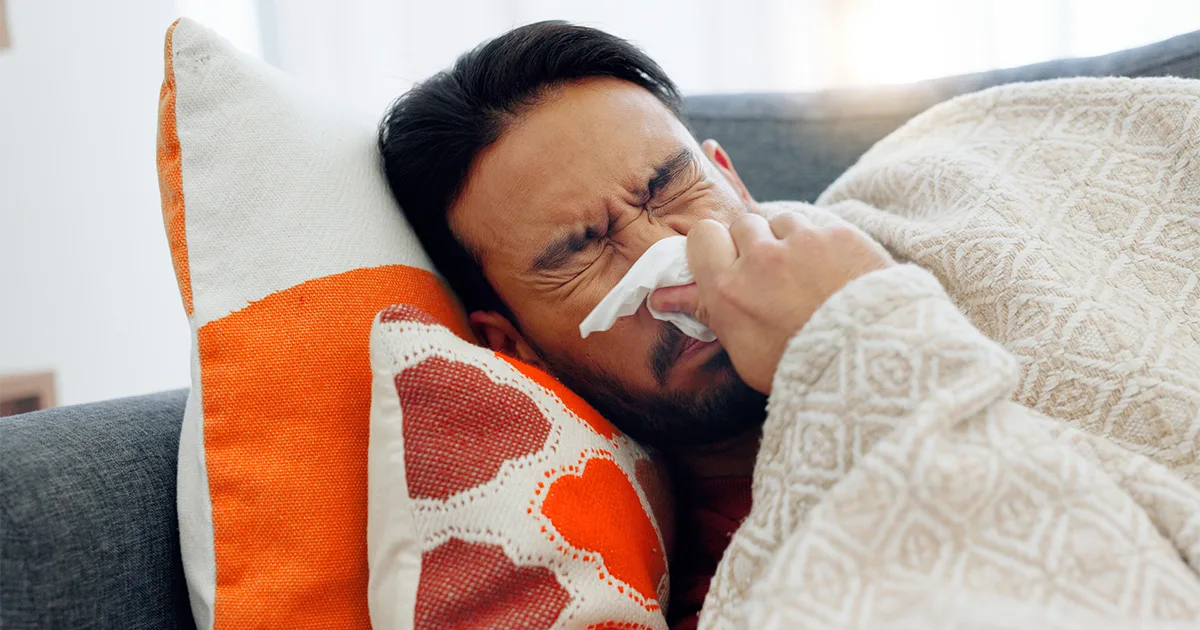 An image of a future vybe urgent care male patient blowing his nose while laying on the couch.