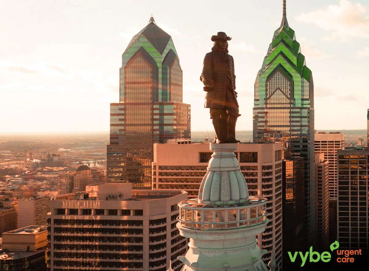 The Philadelphia skyline with a green and orange tint. There is a vybe urgent care logo in the bottom right.
