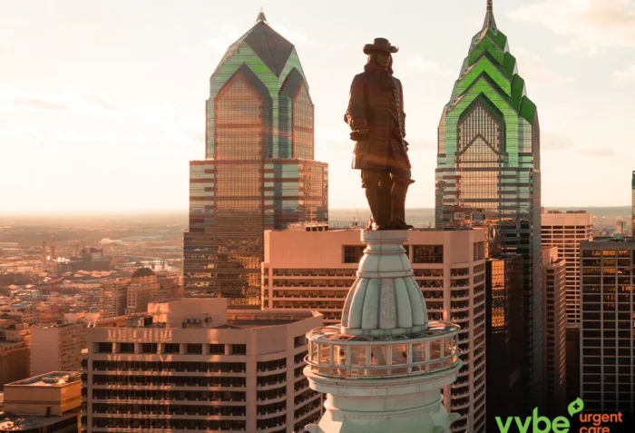 The Philadelphia skyline with a green and orange tint. There is a vybe urgent care logo in the bottom right.
